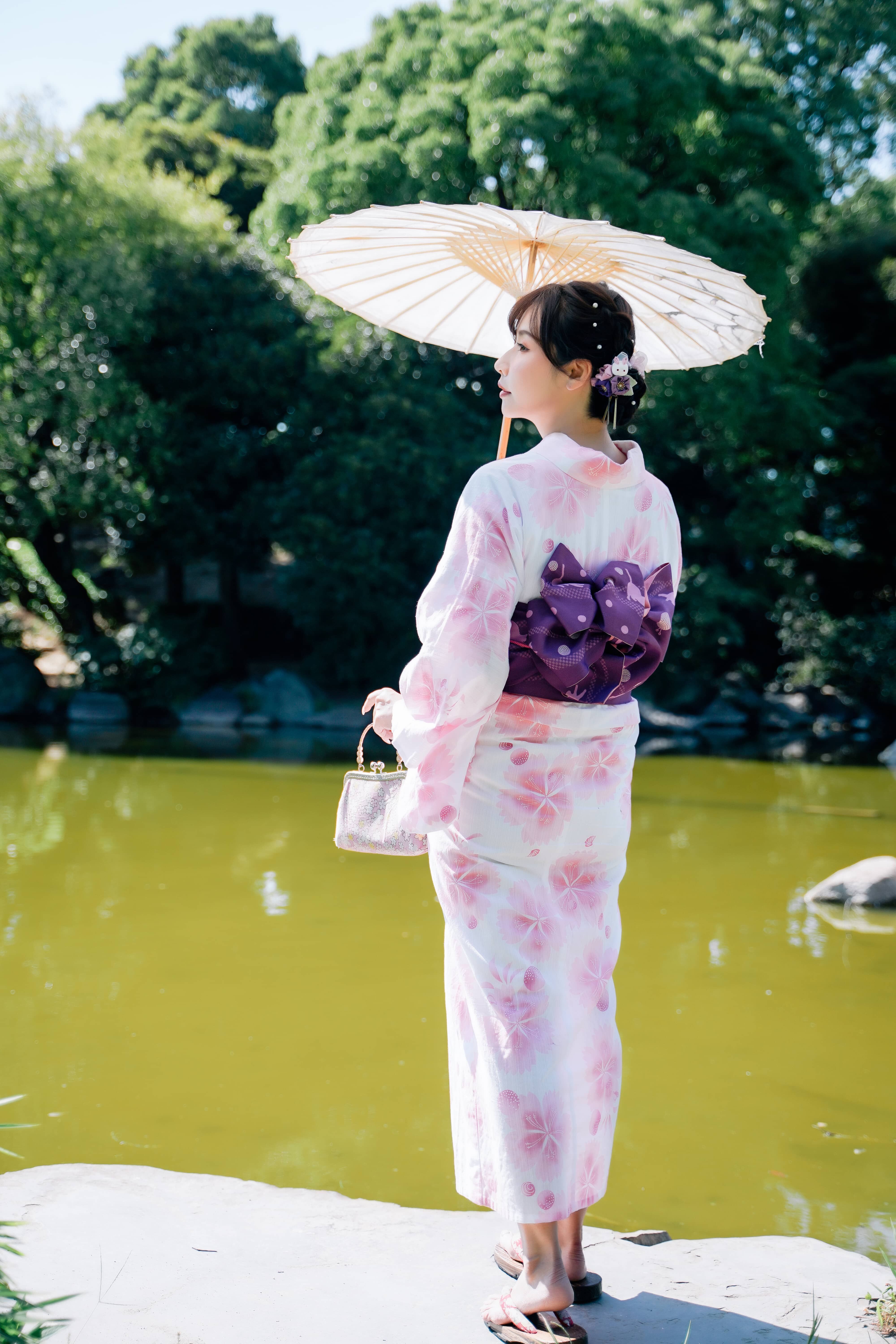 美しく着付けられた浴衣姿の女性が、和傘を差して庭園で佇む後ろ姿